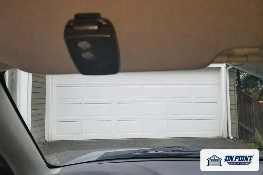 Opener remote clipped to a car visor facing a white garage door