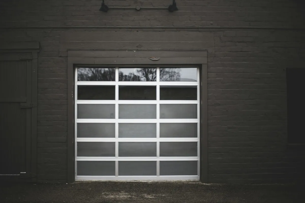 Full-view aluminum and glass garage door set in a dark brick wall
