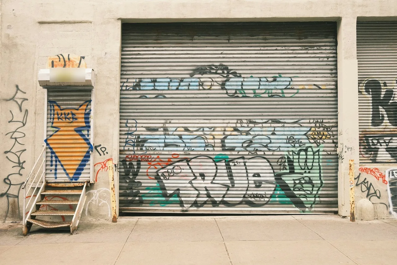 Graffiti-covered rolling gates on a warehouse and a side door, the kind of gate On Point Garage Doors repairs