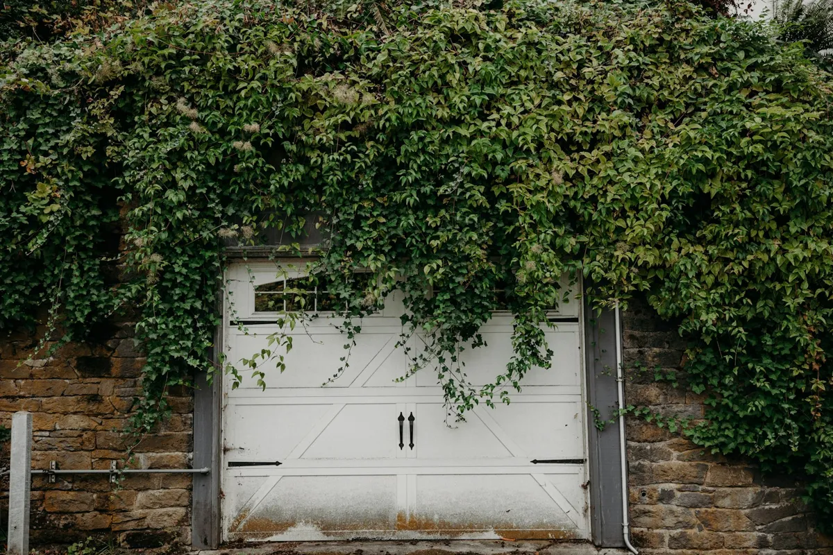 White carriage-house style garage door framed by ivy on a stone wall